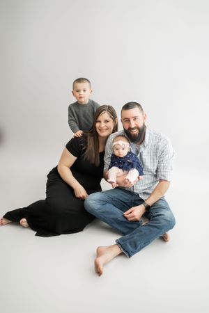 Family of four sitting together on white floor during studio photoshoot.
