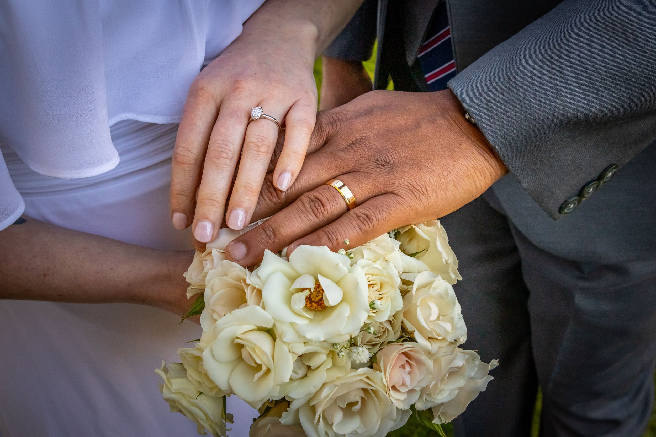 a couple shows off their wedding rings over a bouquet of white roses.