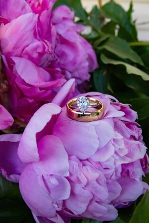 a gold ring and a diamond ring nestled on purple peonies.