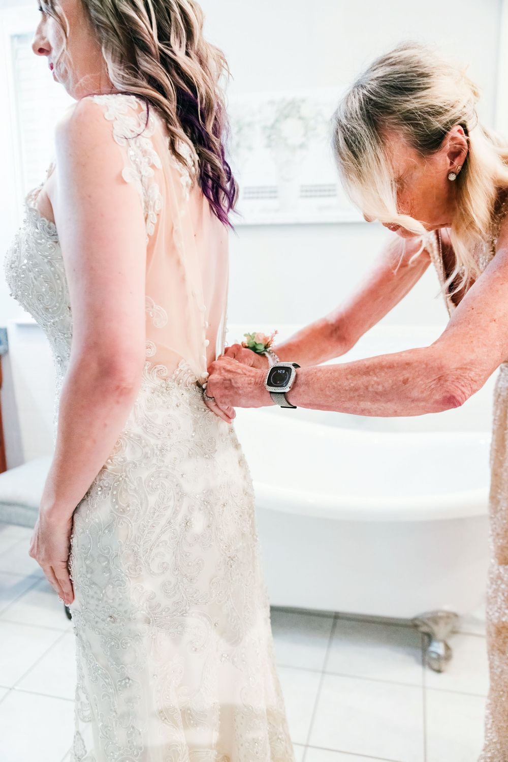 Close-up of a lace wedding dress being fastened by someone wearing a smart watch.