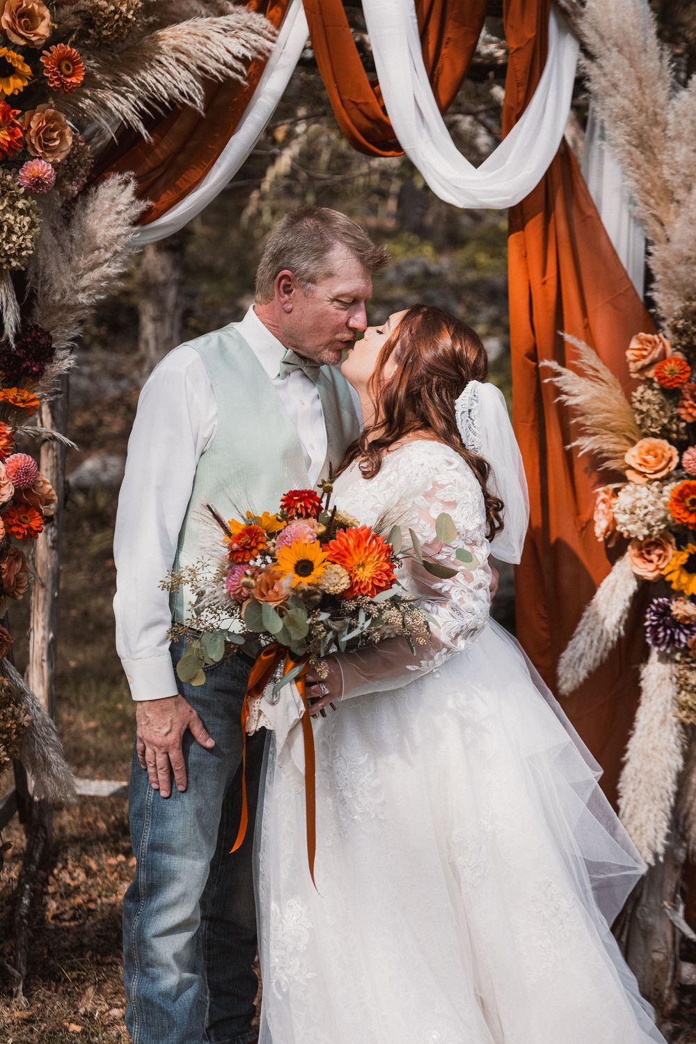Romantic wedding couple embraces under burnt orange arch with sunflower bouquet in autumn woodland setting.