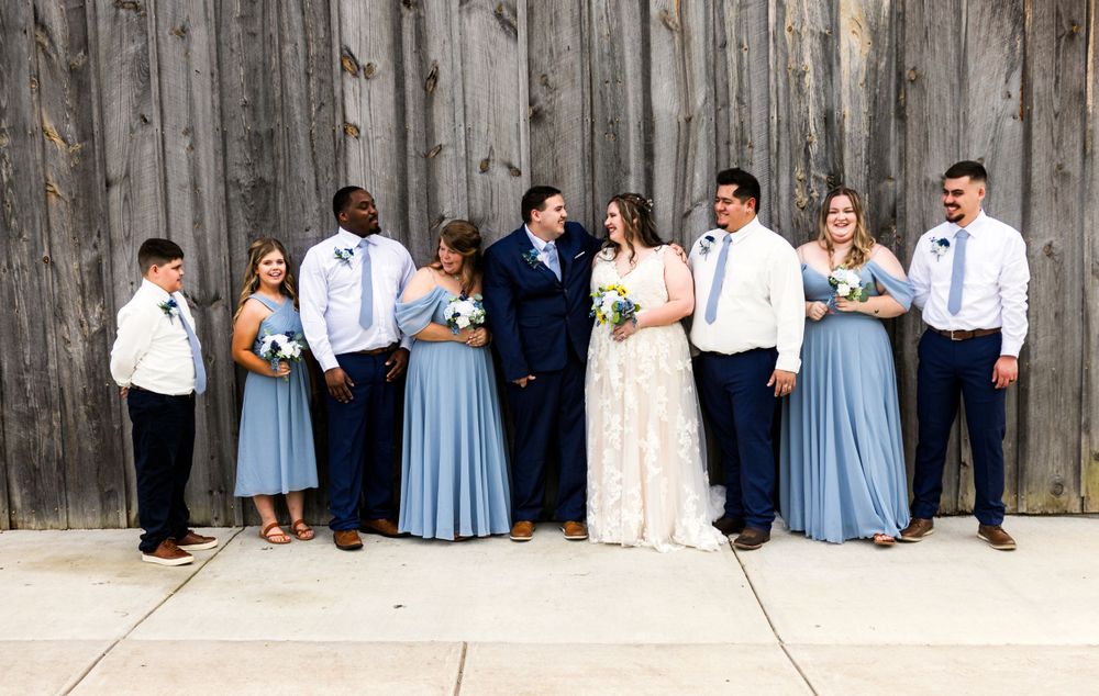 Wedding party poses against rustic wooden wall wearing navy and powder blue attire.