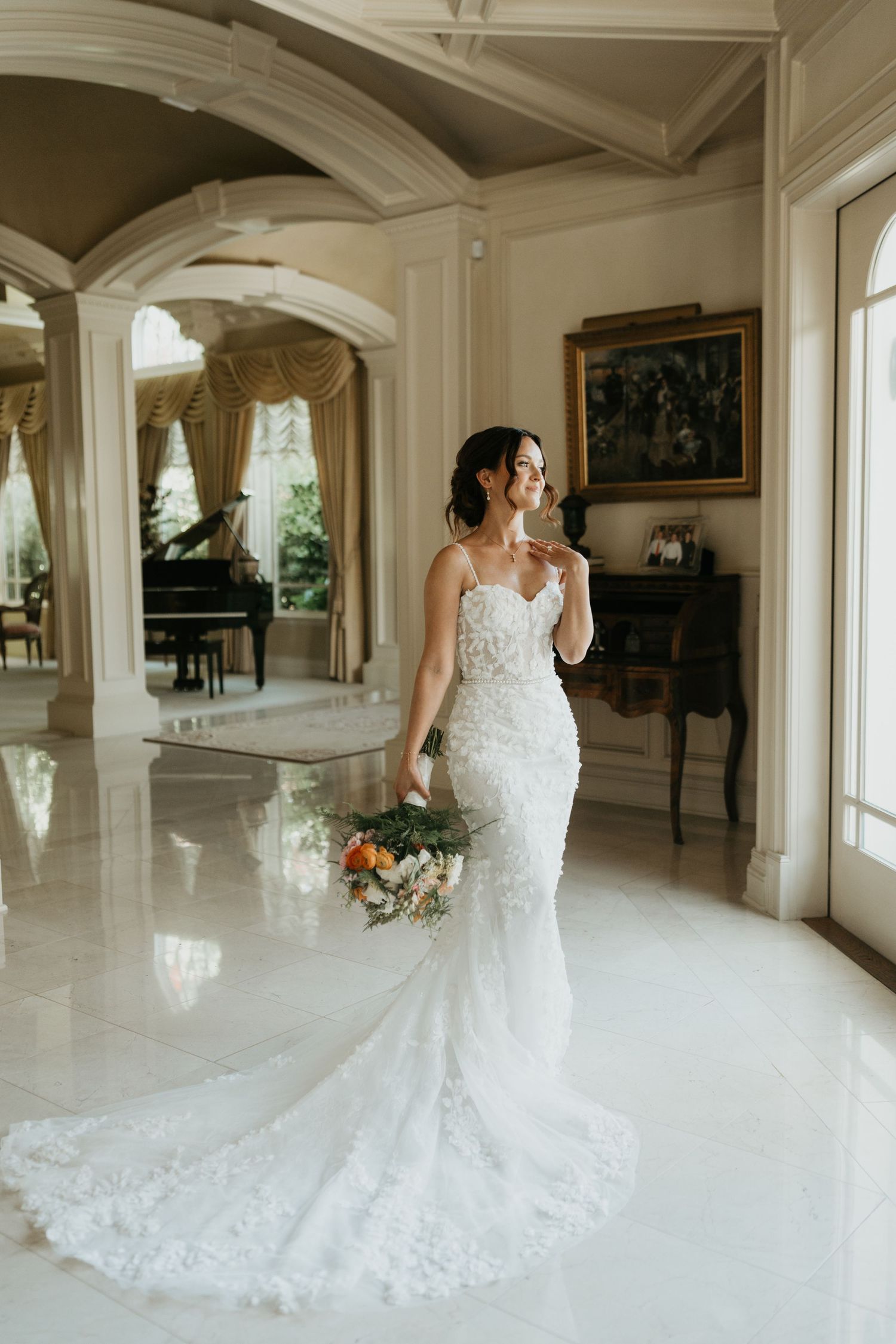 Elegant lace wedding gown with long train photographed in luxurious interior with arched doorways and grand piano.
