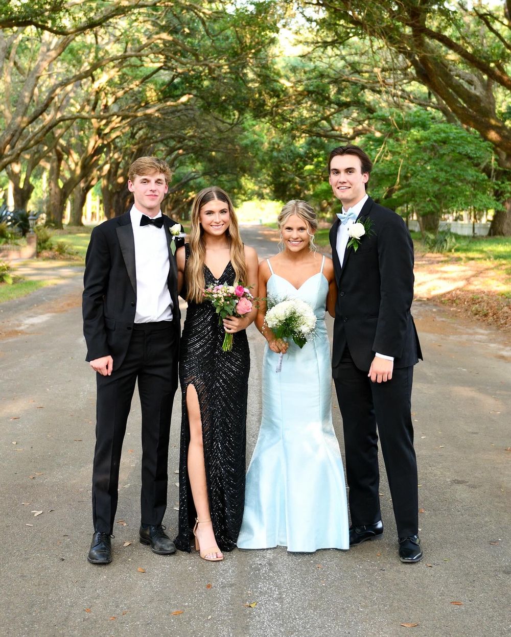 Formal group photo of wedding party standing on a tree-lined path with Spanish moss overhead.