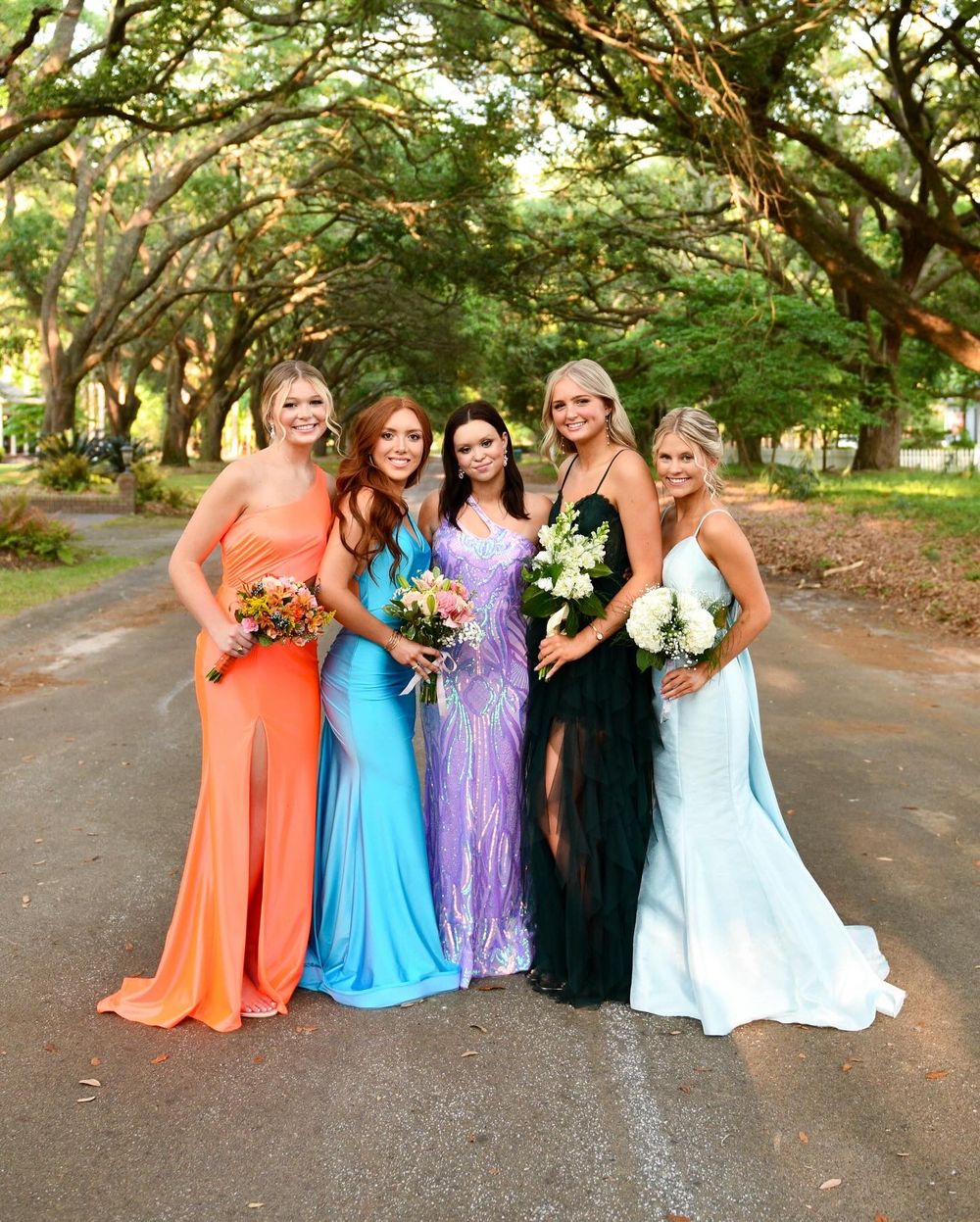 Group of friends in colorful formal dresses posing together for prom or event photos.