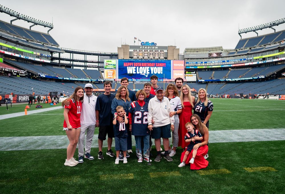 Family group photo on NFL stadium field with scoreboard reading We Love You in background.