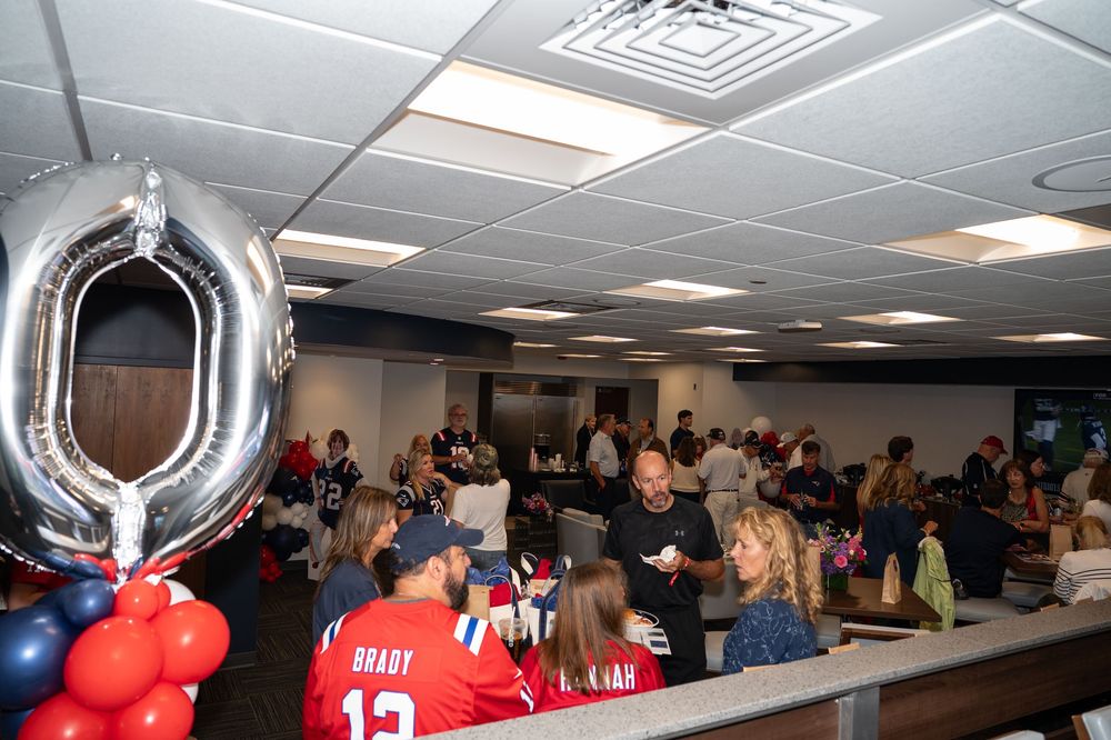 New England Patriots fans gather at a party with Brady jersey, balloons, and a silver number balloon decoration.