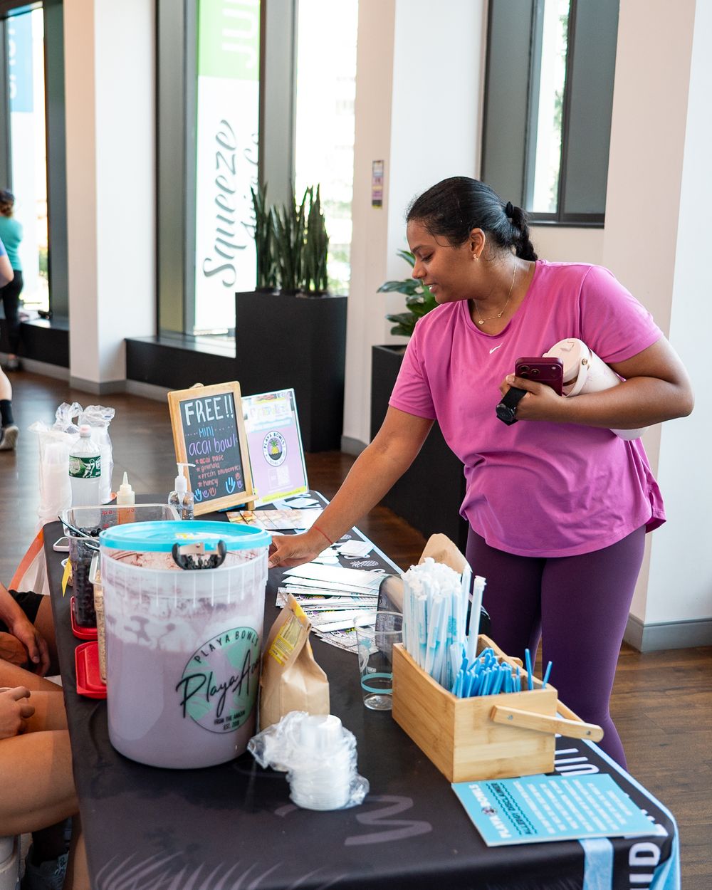Woman in pink top browses wellness products at a free event table inside a modern fitness studio.
