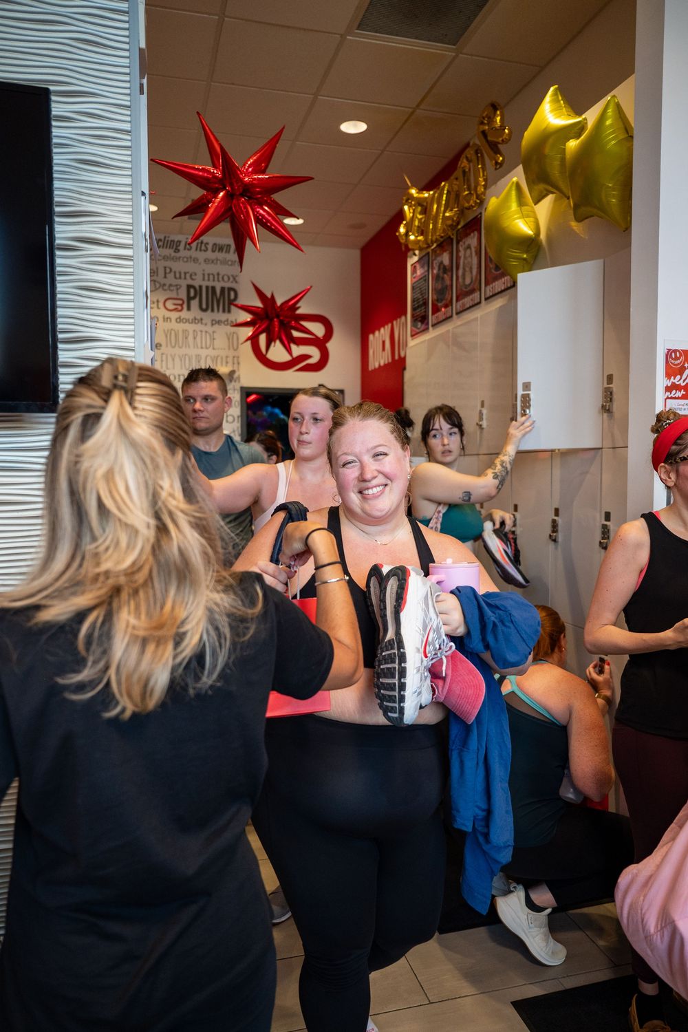 Women celebrating in a gym lobby with red and gold star balloons decorating the festive indoor space.
