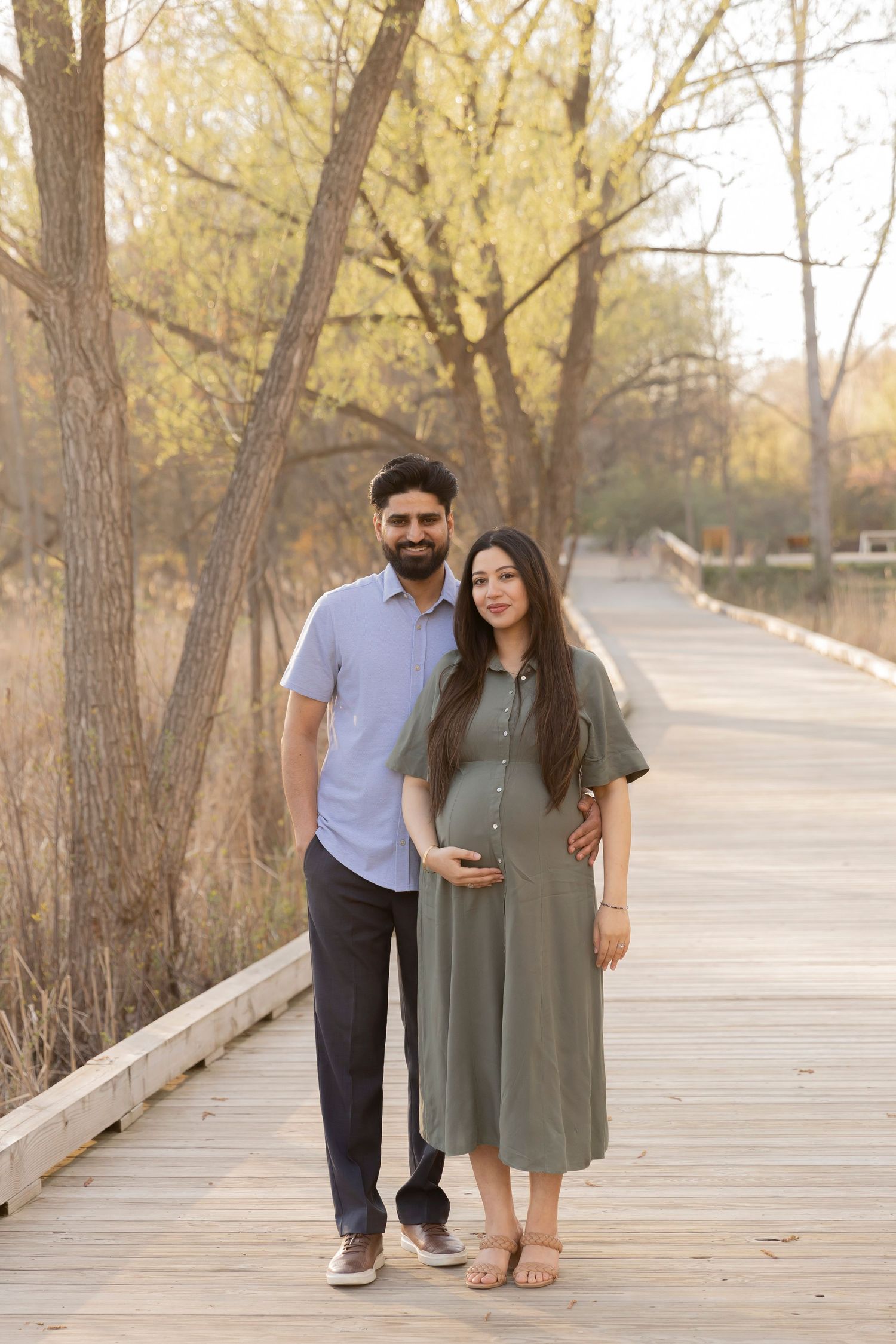 pregnant couple posing for a photo on a wooden walkway in Rochester Hills michigan
