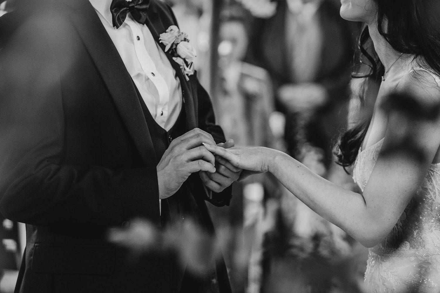 Intimate black and white close-up of ring exchange during wedding ceremony.