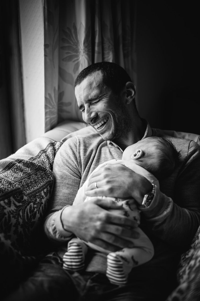 Father laughing joyfully while holding his newborn son, capturing a father-child bonding via a newborn photography.