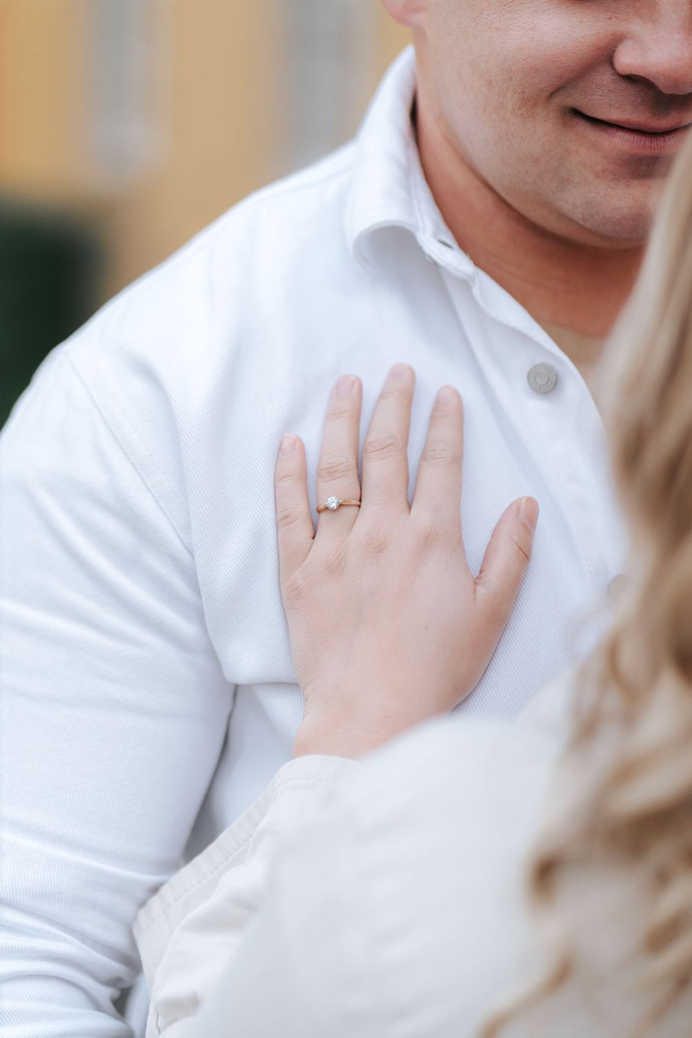 Close-up of engagement ring as hand rests on white shirt.