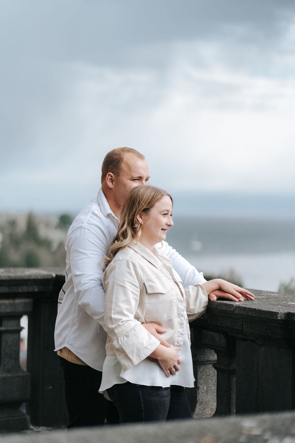 Couple embraces at stone overlook with misty coastal view.