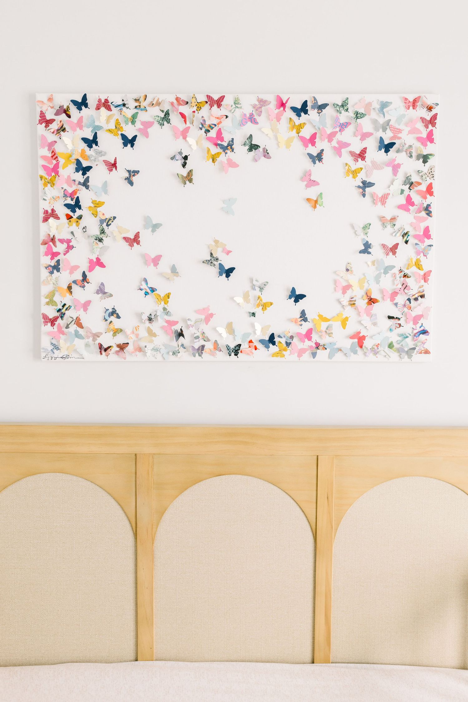 Colorful butterfly art print hanging above a wooden crib in a nursery.