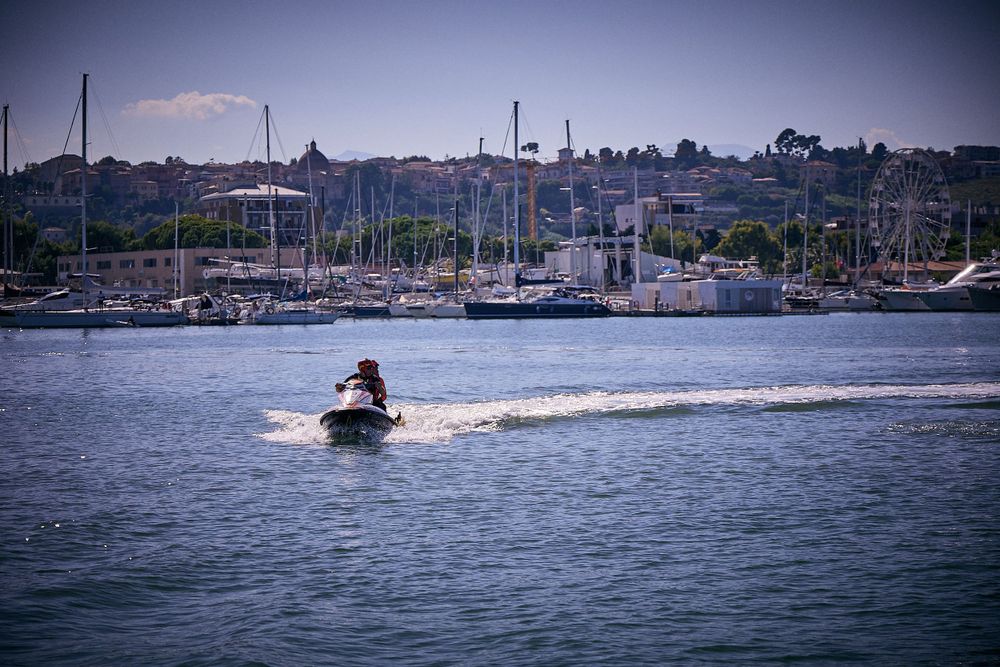 Jet ski rider creates wake across marina harbor with boats and hills in background.