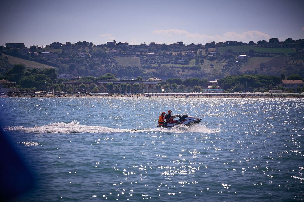 Jet ski sprays water across sparkling bay with coastal homes in background.