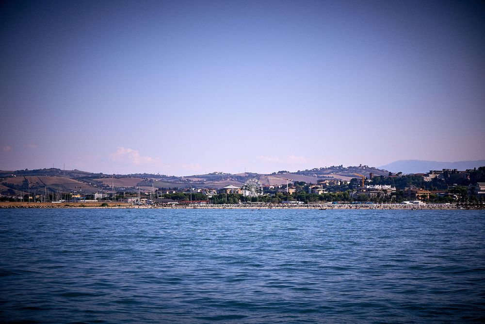 Coastal cityscape view with mountains and buildings along shoreline under clear blue sky.