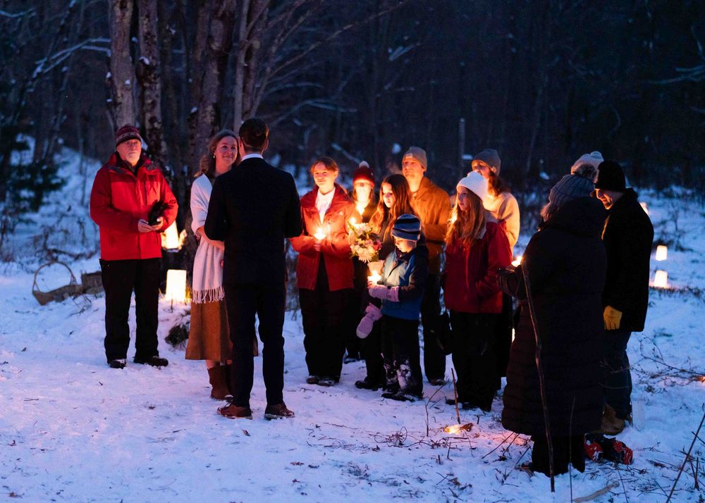A group of people stand in a circle holding candles during a nighttime winter ceremony.