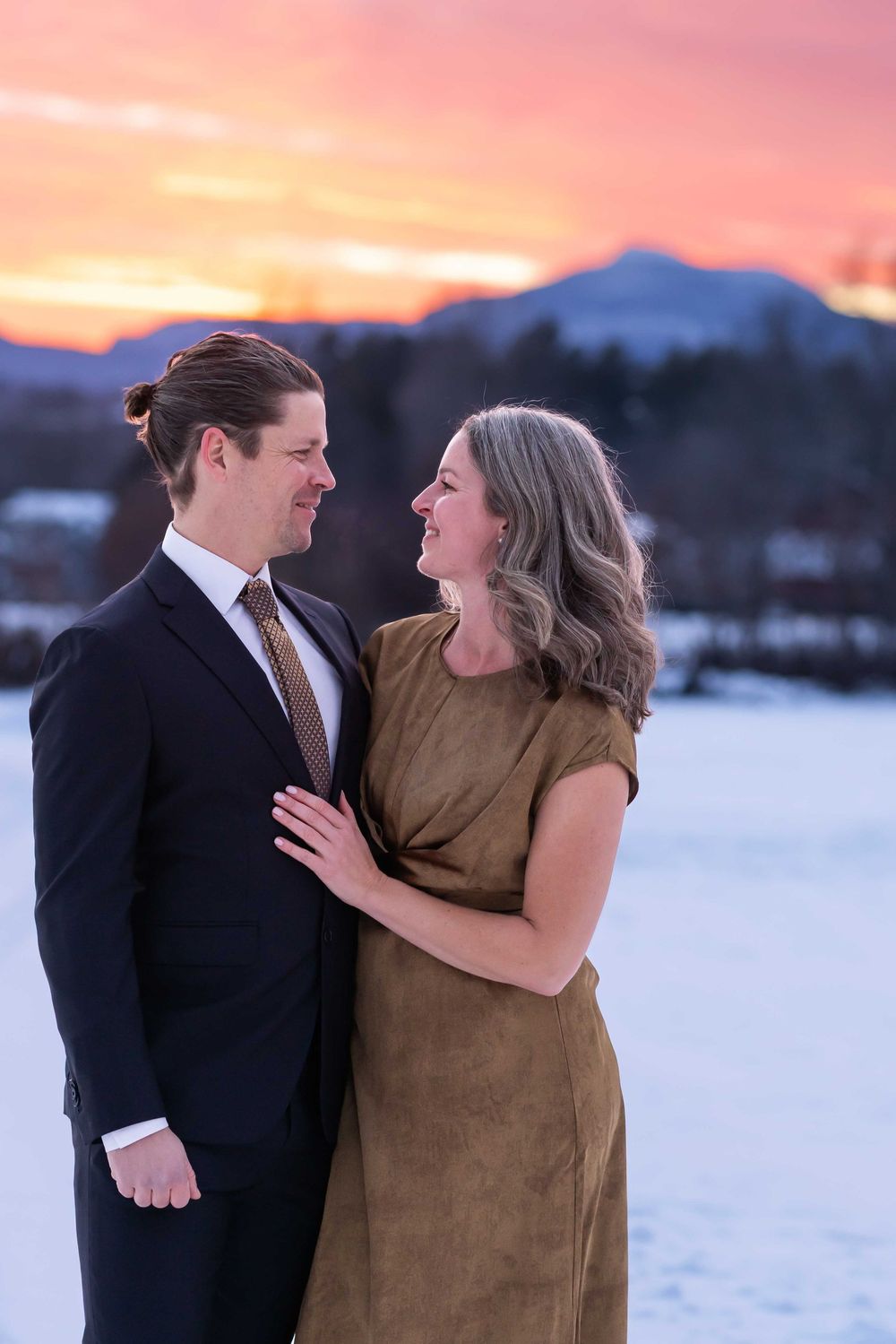 A couple shares a tender moment against a snowy winter backdrop during sunset.