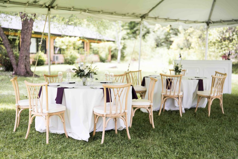 Elegant outdoor wedding reception setup with white tables and gold chairs under a white tent.