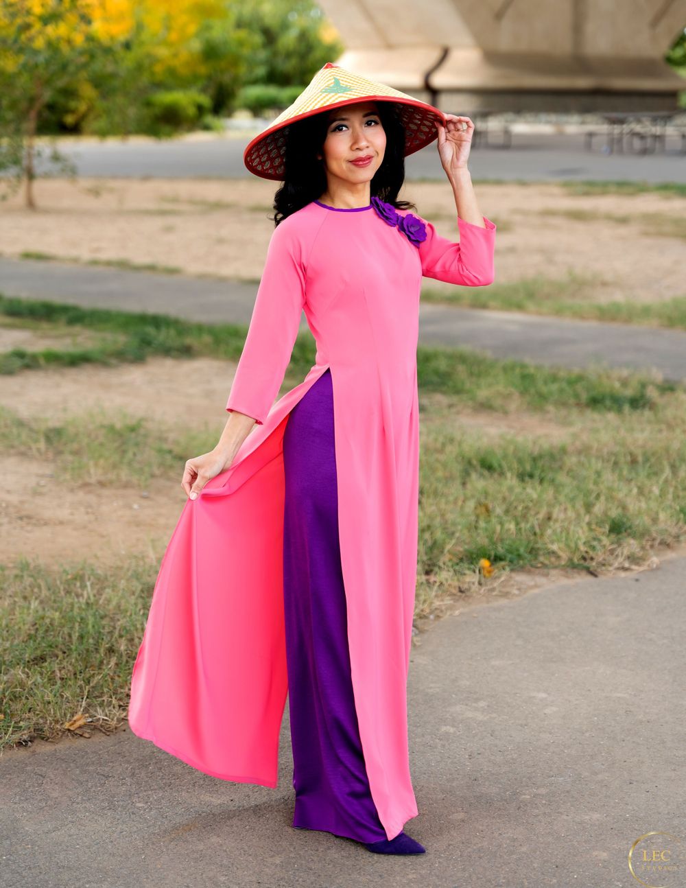 Traditional female Vietnamese style ao dai dress in bright pink and purple worn with conical hat on outdoor path.