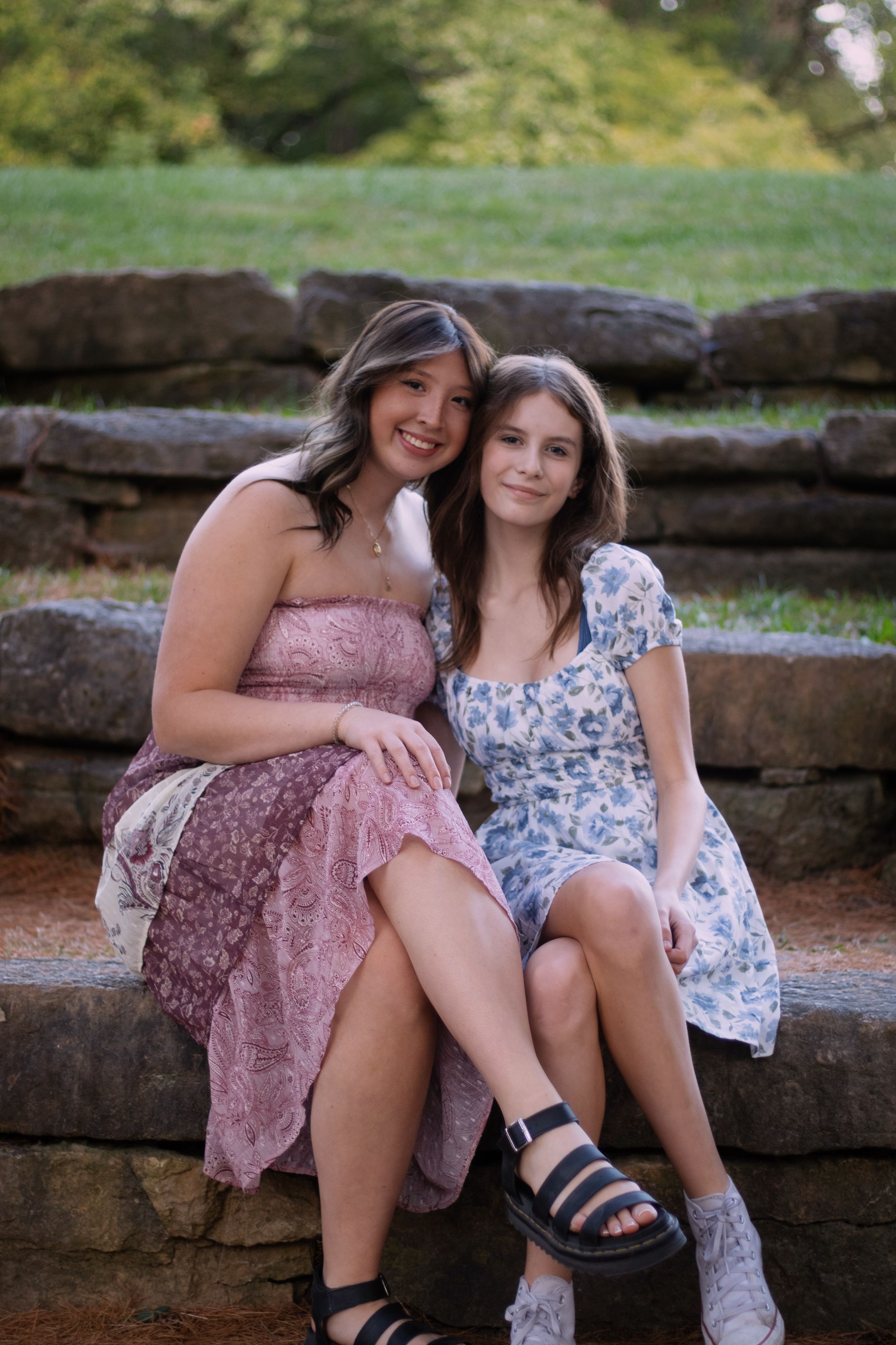Two girls hugging eachother sitting outside at a park on a stone bench