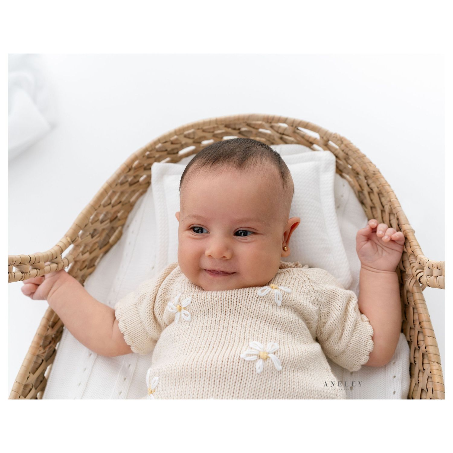 Smiling baby in cream sweater lying in woven basket during photo shoot.