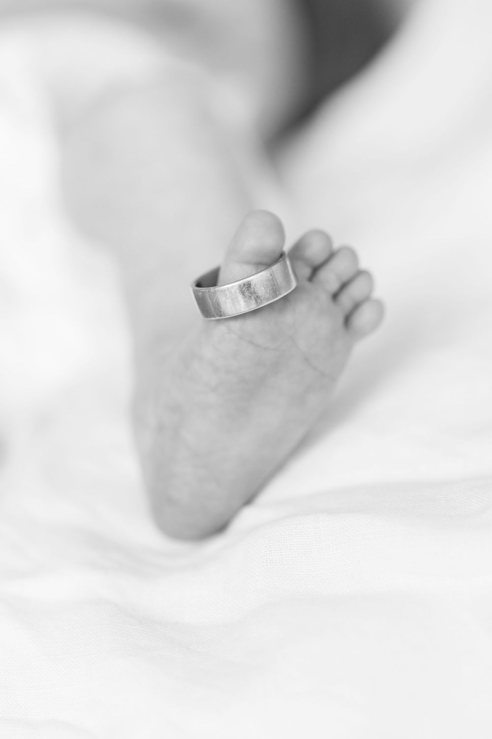 Close-up of a baby's tiny toe adorned with dad's wedding band, symbolizing love and family connection in a tender moment.
