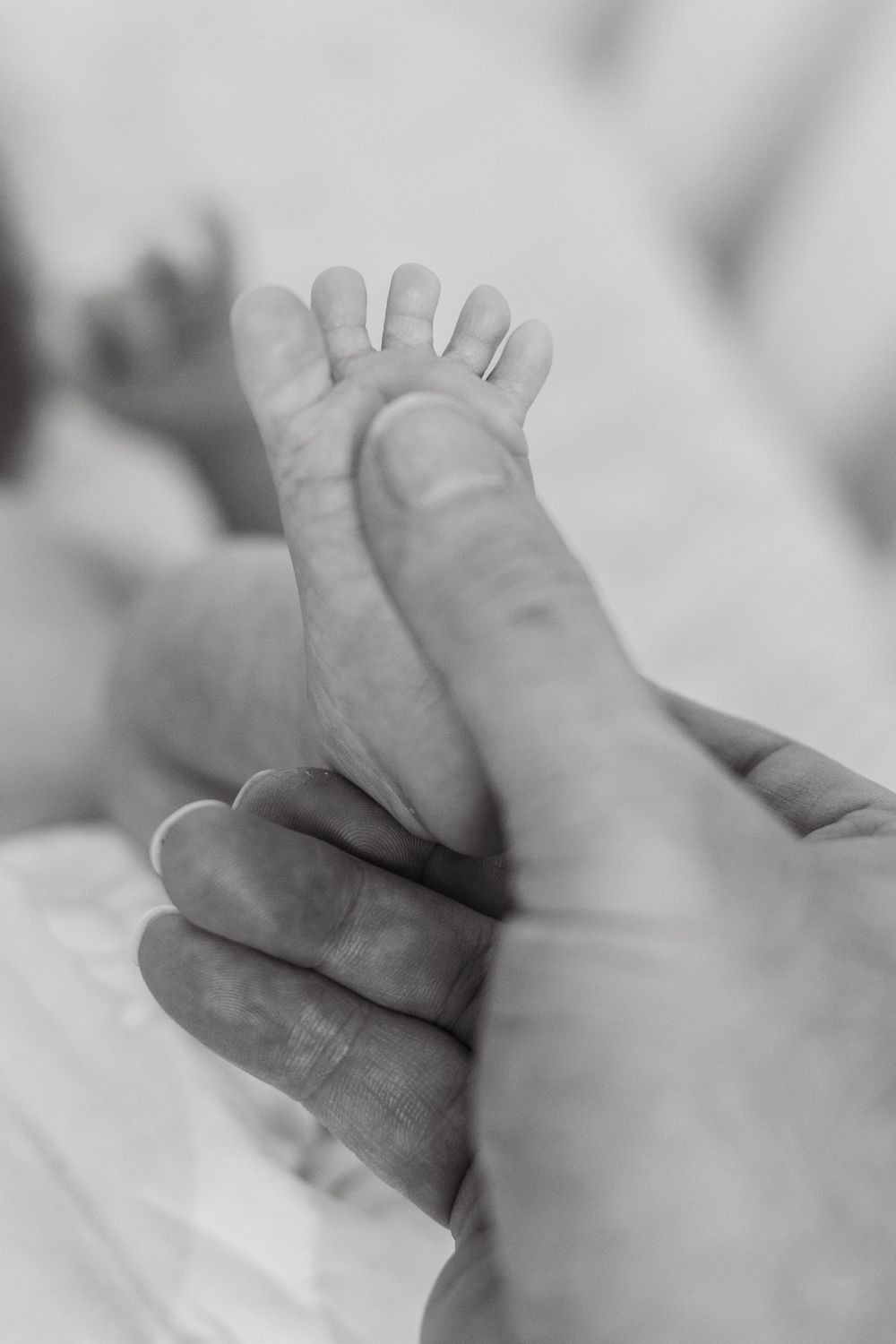 Close-up of a baby's tiny feet with dad's thumb gently holding them, showcasing a tender moment of parental love.