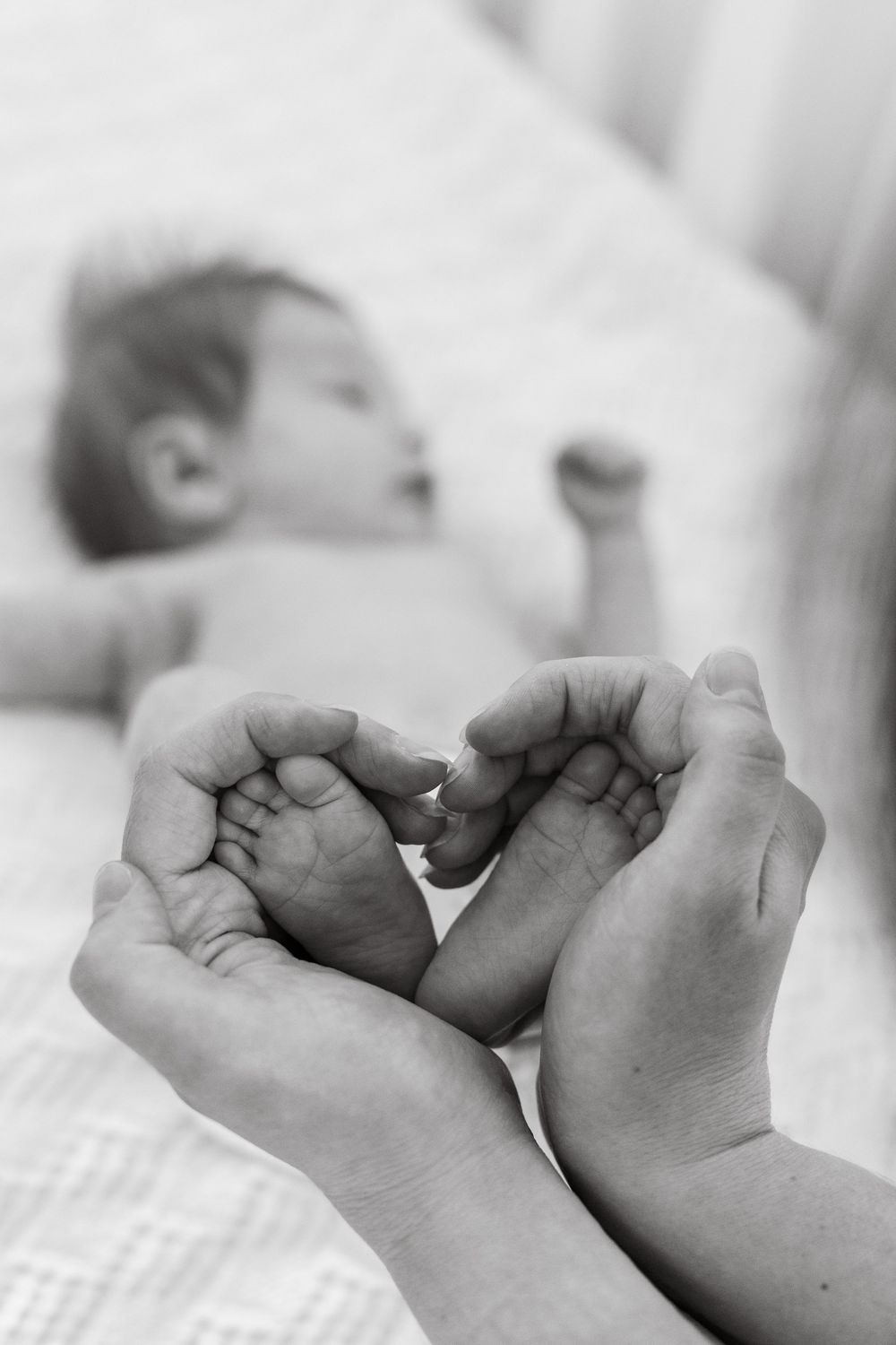 Close-up of a baby's tiny feet gently held by mom's hands, forming a heart shape, symbolizing love and care.