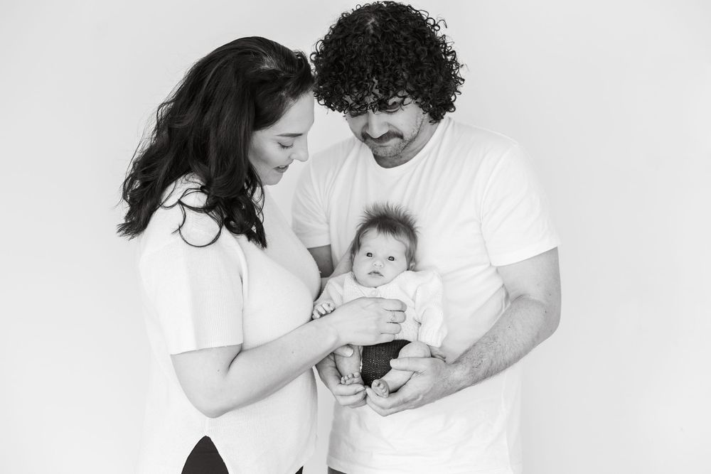Mom and dad lovingly holding their newborn baby, smiling warmly in a cozy family moment.