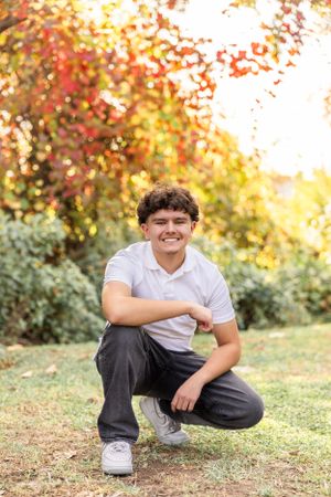 Student poses casually on autumn grass with fall foliage in background.