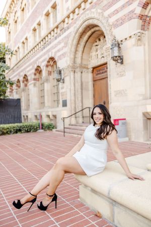 Graduate in white dress poses on architectural steps of historic building.