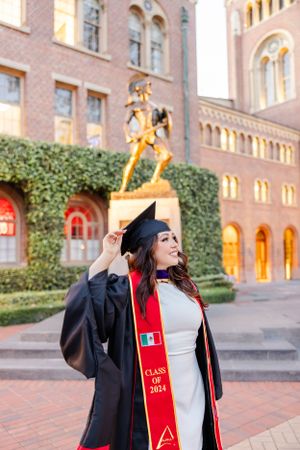 Graduate in cap and gown celebrating with diploma on university campus.