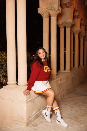 Graduate in USC attire posing between classical white columns.