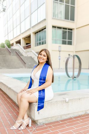 Graduate in blue graduation sash poses near modern building with pool.