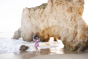 Person walking along scenic beach with dramatic rock formations and crashing waves.