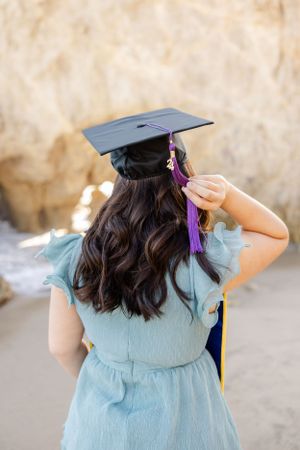Graduation photos at the beach featuring teal dress and traditional cap with purple tassel.