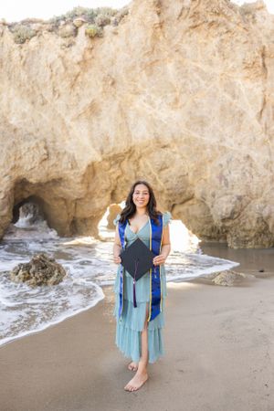 Woman in turquoise dress poses against coastal rock formations at a scenic beach.