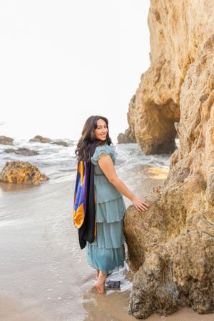 Woman explores rocky beach caves while wearing a flowy turquoise outfit.