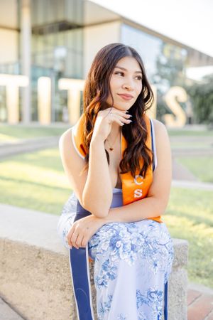 Graduate in orange and blue athletic wear poses elegantly on campus grounds.