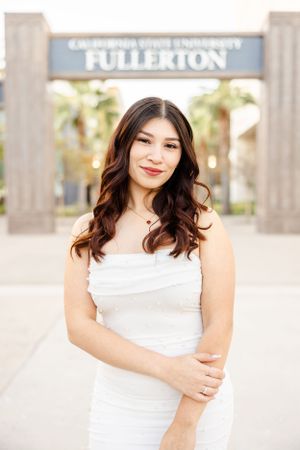 Graduate poses in white dress at Cal State Fullerton entrance sign.