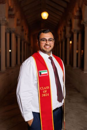 Graduate in formal attire and red stole stands confidently in historic columned hallway.