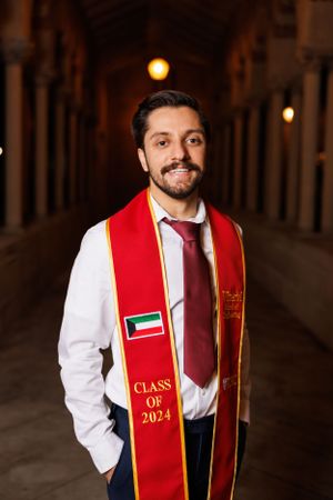 Graduate wearing Class of 2024 red graduation stole poses in ornate hallway with arched columns.