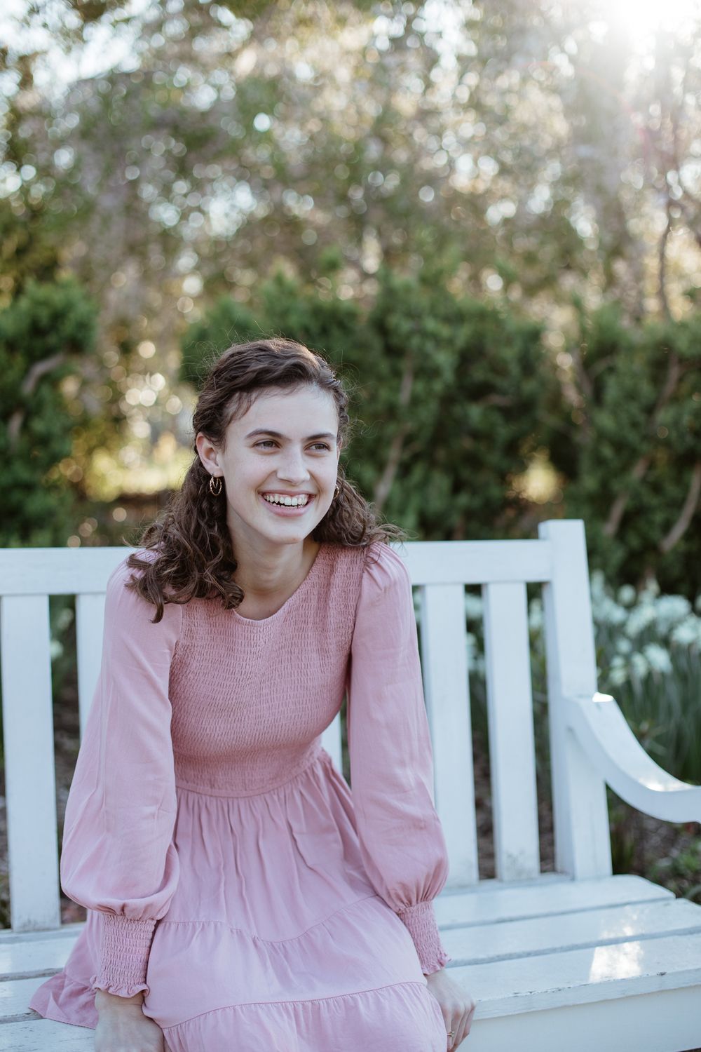 Joyful springtime portrait on white garden bench surrounded by greenery.