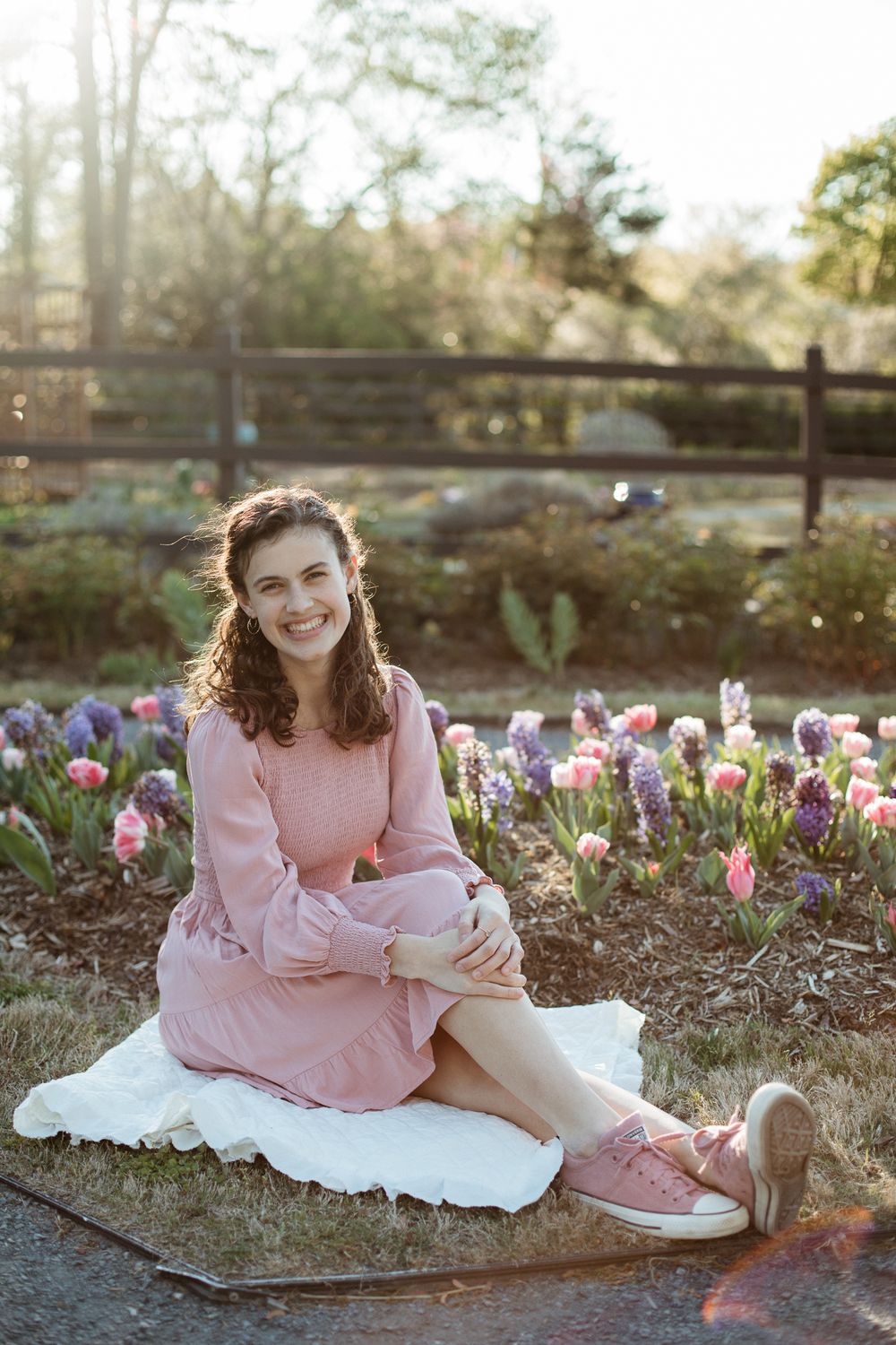Person in pink dress sits on blanket among blooming spring tulips.