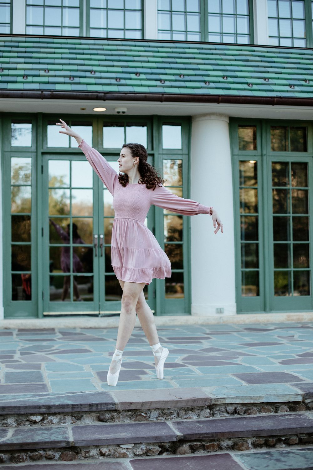 Ballet dancer in pink dress performs en pointe outside classical building.