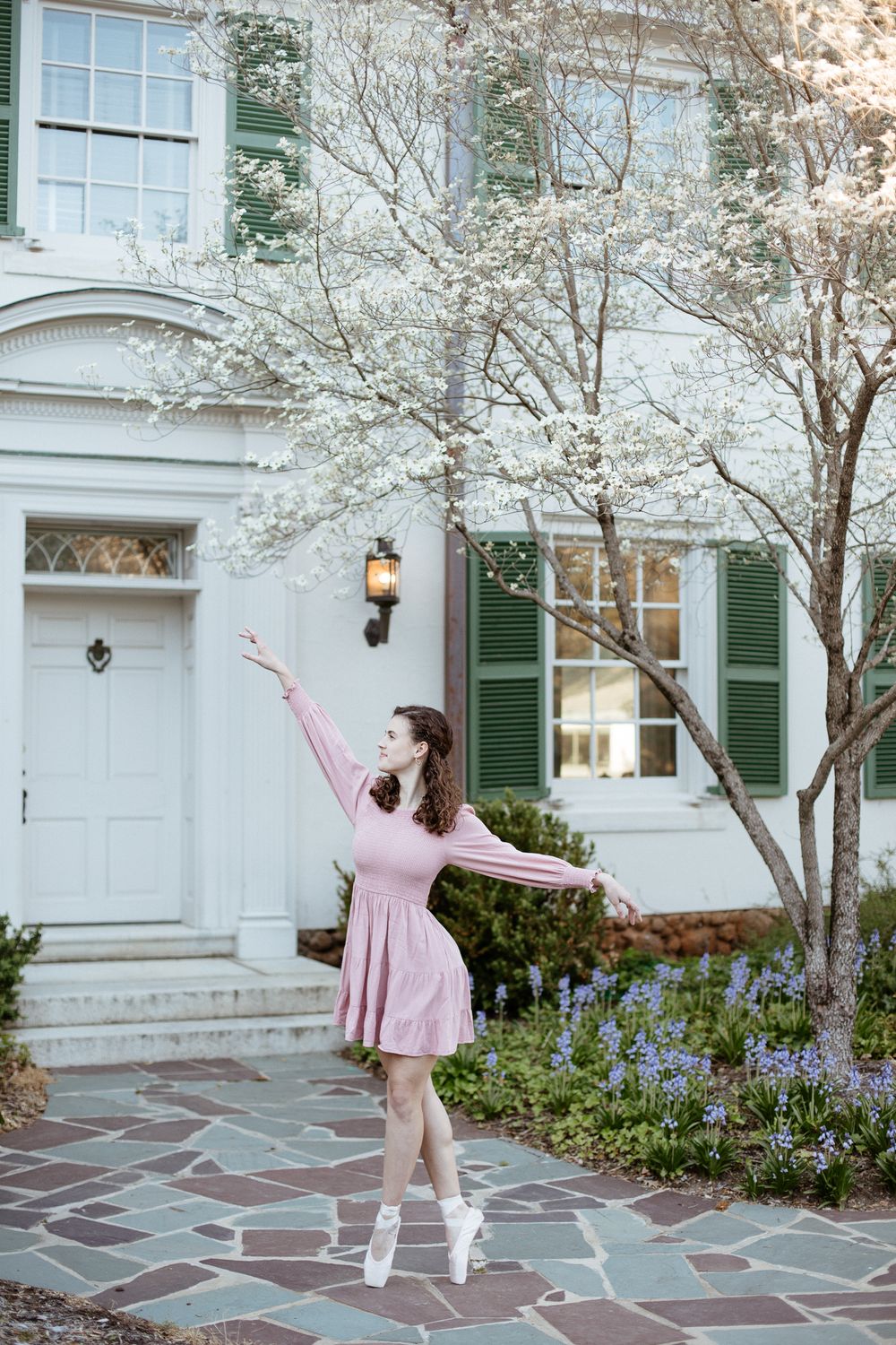 Dancer in pink dress poses gracefully beneath blooming spring trees.