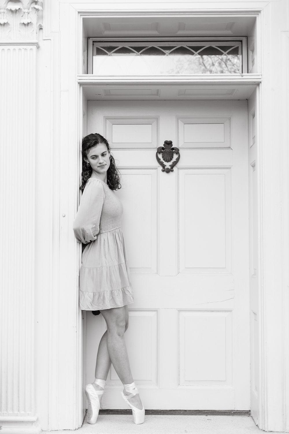 Ballet dancer in white dress poses elegantly against white doors in monochromatic photo series.